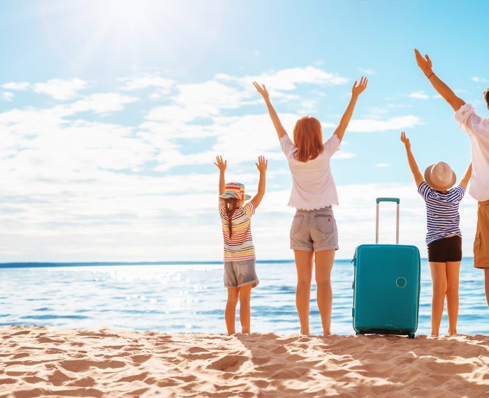 Mother and father with their children standing on the beach with suitcases.