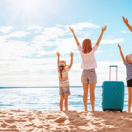 Mother and father with their children standing on the beach with suitcases.